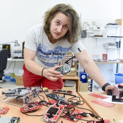 A younger Albert Gajšak leaning over a workbench covered in red circuit boards and prototypes.