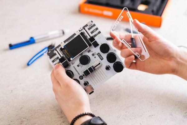 Two hands fitting a clear acrylic top plate onto a part-built Jay-D DJ mixer, its circuit board and pads exposed.