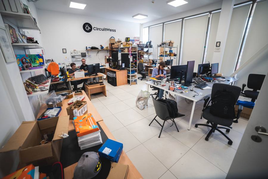 Wide interior of the CircuitMess office: workbenches, shelved parts, a 3D printer and the CircuitMess wordmark on the far wall.